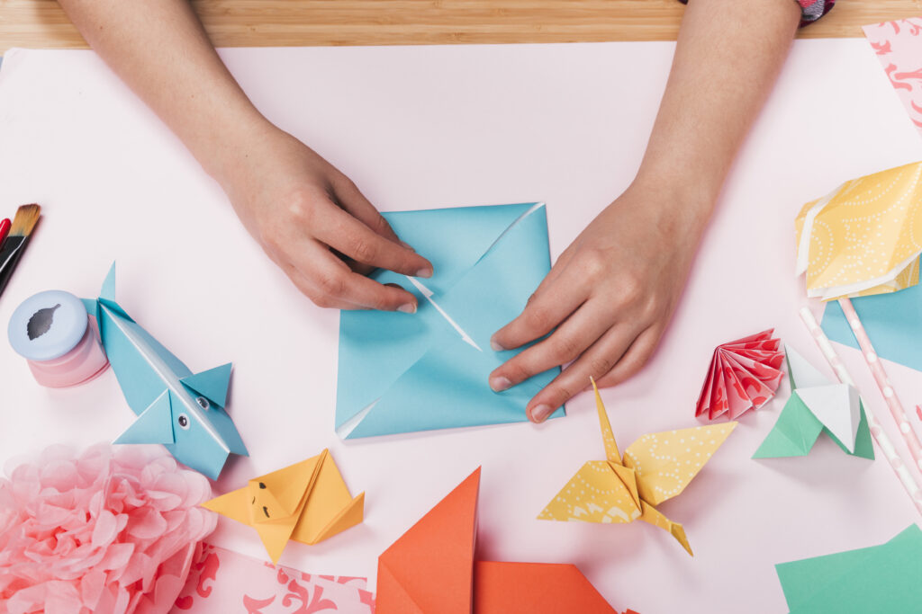 vista-superior-mano-mujer-que-hace-arte-origami-sobre-tabla